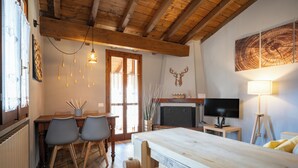 A cozy room with a wooden ceiling, a fireplace, a television, and a dining area with chairs and a table.