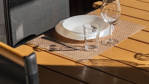 A dining table set with a white plate, a glass, and a fork, with a woven placemat.