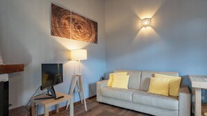 A living room with a sofa, a floor lamp, a TV, and a wall-mounted light fixture.