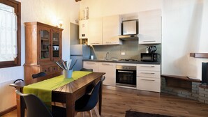 A compact kitchen with a dining area, featuring a wooden table, chairs, a cabinet, and modern appliances. - La Corte della Casera - Verbena (Cremeno)