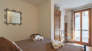 A bedroom with a bed, a mirror, a wooden wardrobe, a chair, and a window with curtains. - La Corte della Casera - Verbena (Cremeno)