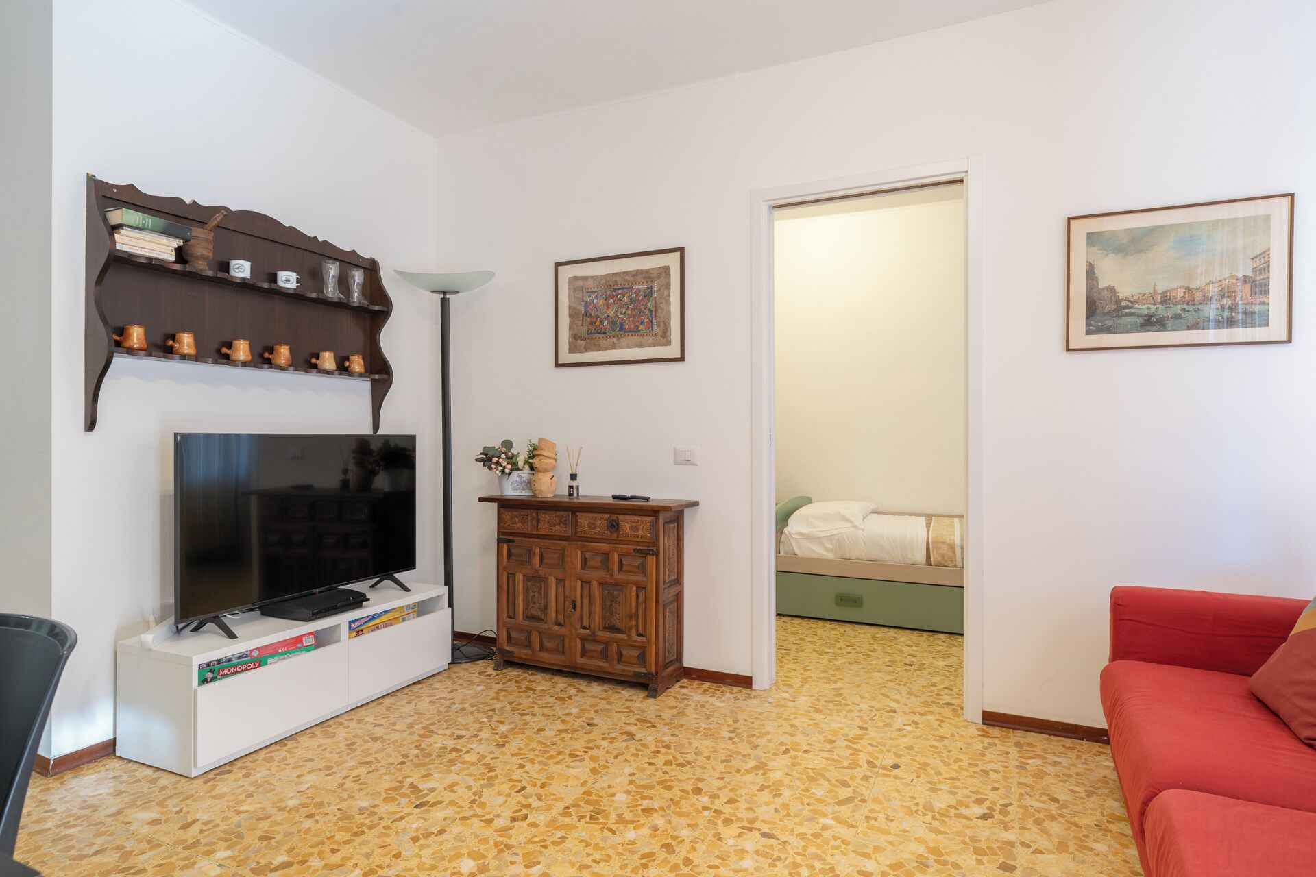 A living room with a television, a cabinet with decorative items, a red sofa, and a door leading to another room.