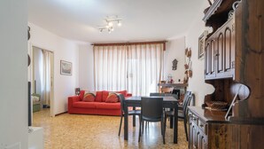 Una sala de estar con un sofá rojo, una mesa de comedor con sillas, y una zona de cocina con armarios de madera.