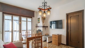 Una sala de estar con sofá, una mesa de centro, una zona de comedor con mesa y sillas, un televisor montado en la pared y una puerta.