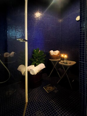 A bathroom with blue mosaic tiles, a glass shower enclosure, a plant, towels, and candles. - Ampio monolocale con bagno turco (Cremeno)