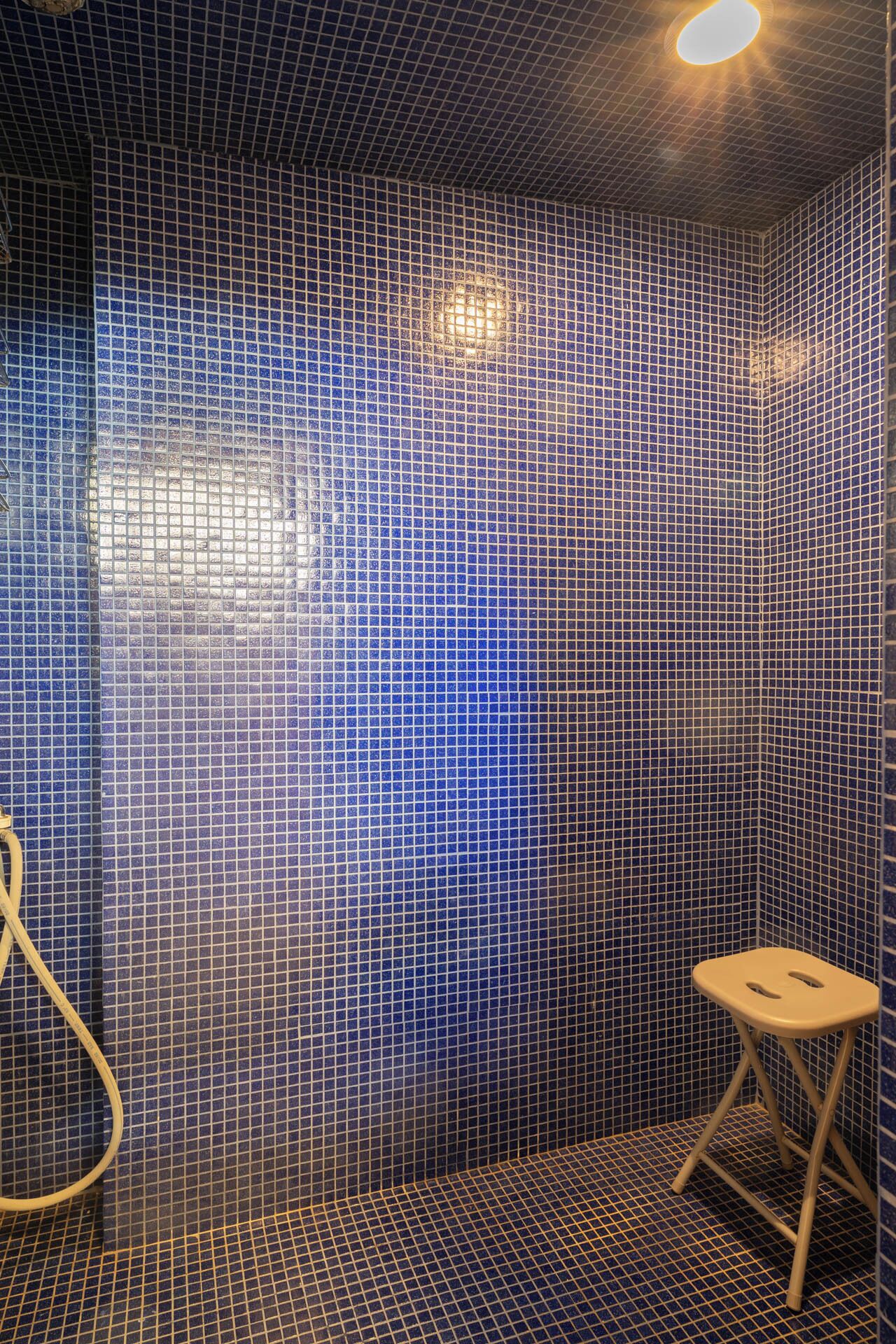 A bathroom with blue mosaic tiles, a step stool, and a light fixture.