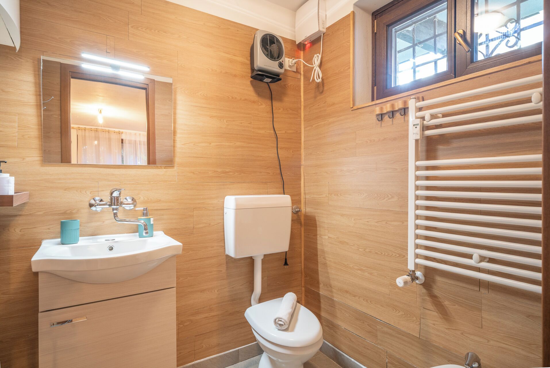 Ein modernes Badezimmer mit einer Holzwand, einem weißen Waschbecken, einer Toilette und einem Handtuchhalter.