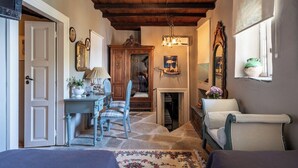 A cozy room with a stone floor, a wooden ceiling, a desk with a chair, a fireplace, and a window with a plant. - Seaside Neoclassical Property in Vaporia Ermoupoli (Syros)
