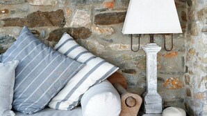 A stone wall, a wooden bench with cushions, a white lamp, and a hat on a small wooden table. - Seaside Neoclassical Property in Vaporia Ermoupoli (Syros)