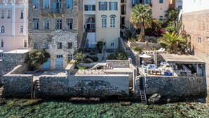 A coastal building with stone walls, a staircase leading to upper floors, and outdoor seating areas with umbrellas. - Seaside Neoclassical Property in Vaporia Ermoupoli (Syros)