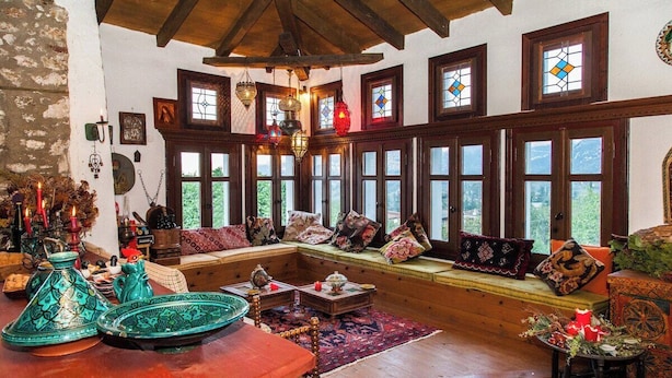 A cozy living room with a wooden bench, colorful cushions, and a view through large windows. - 260m2 Unique Mountain House in Lilea Parnasos (Delphi)