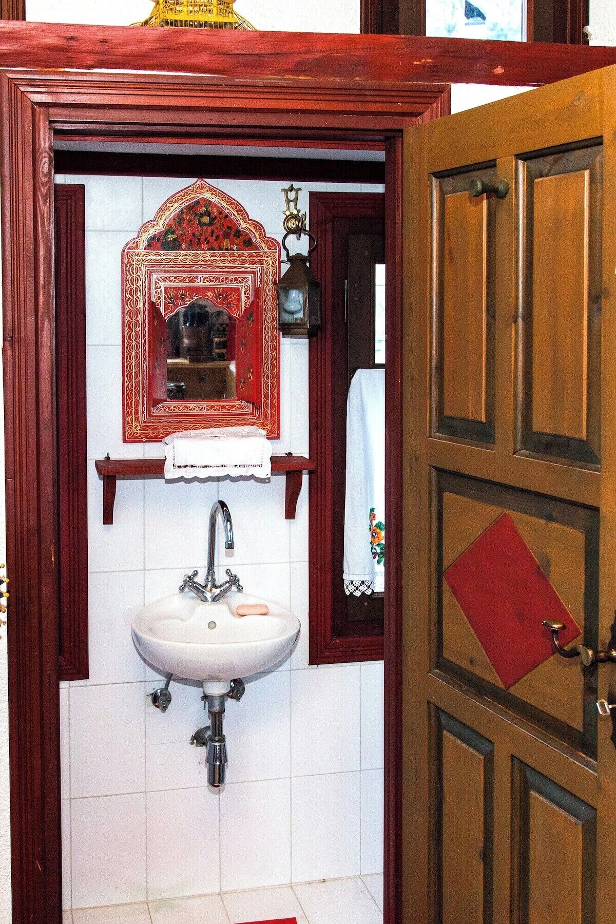 Une salle de bain avec un lavabo blanc, un miroir doté d’un cadre décoratif et une serviette rouge accrochée au mur.