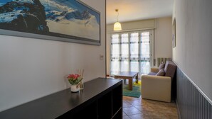 A living room with a sofa, a table, and a painting of a mountain scene. - Piani di Bobbio Adventure Base (Cremeno)