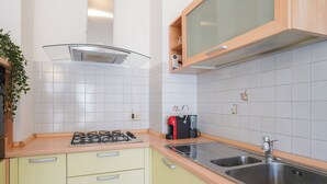 A kitchen with a gas stove, two sinks, a coffee maker, and a cabinet with a glass door. - Piani di Bobbio Adventure Base (Cremeno)