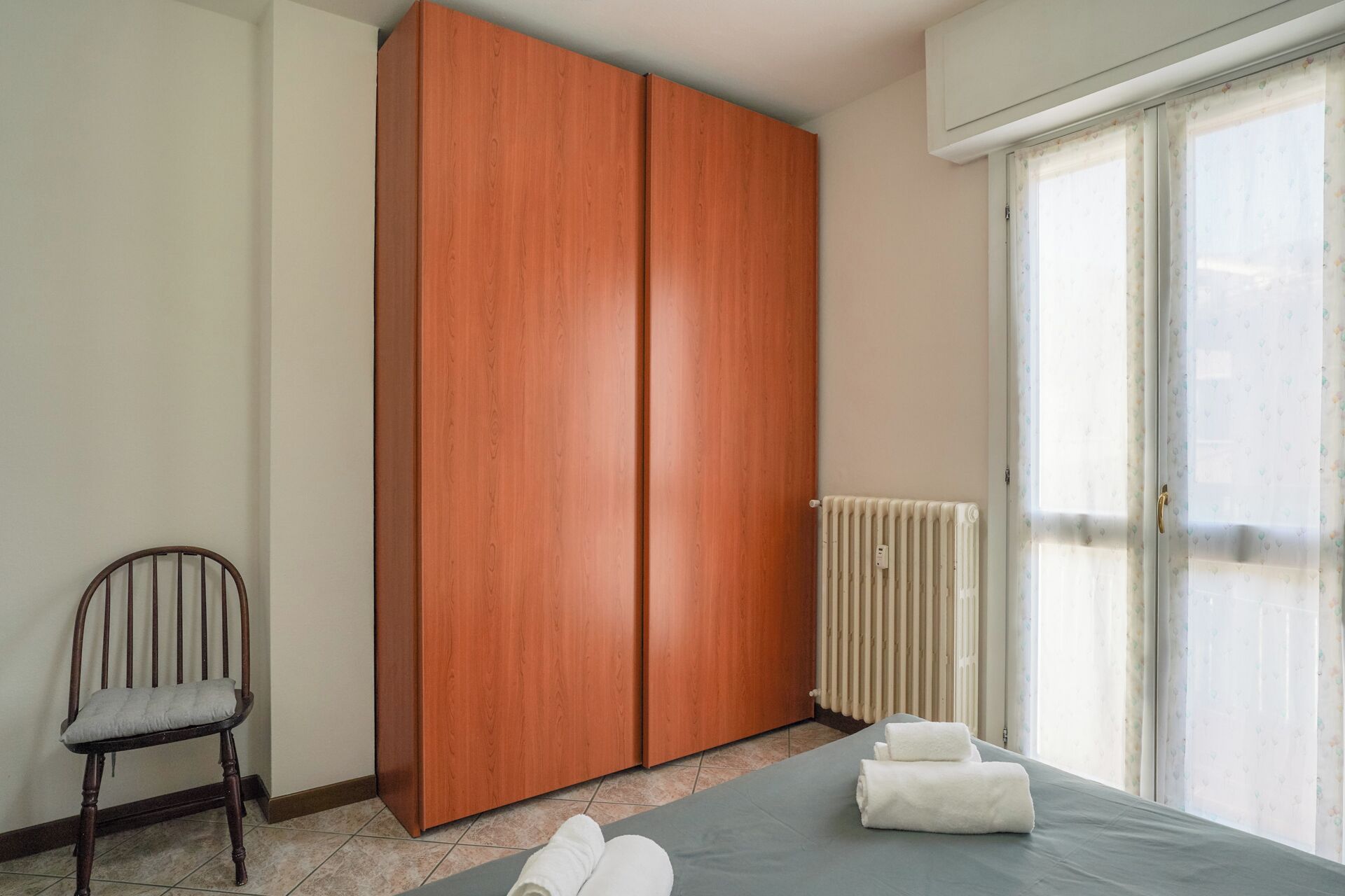 Camera da letto con un armadio grande, un termosifone, una sedia e un letto con asciugamani.