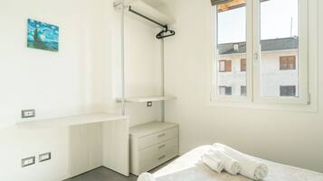 A minimalist bedroom with a bed, a hanging rack, and a window with a view of buildings.
