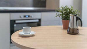 Ett runt träbord med en vit kopp och ett tillhörande fat samt en kaffekanna i rostfritt stål.