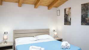 A neatly made bed with a blue bedspread and white pillows, two bedside lamps, and a wall with two framed pictures. - Residence San Rocco - Appartmento Resegone (Cremeno)