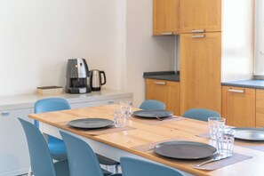 Een eetgedeelte met een houten tafel gedekt voor vier personen, blauwe stoelen en een koffieapparaat op de achtergrond.