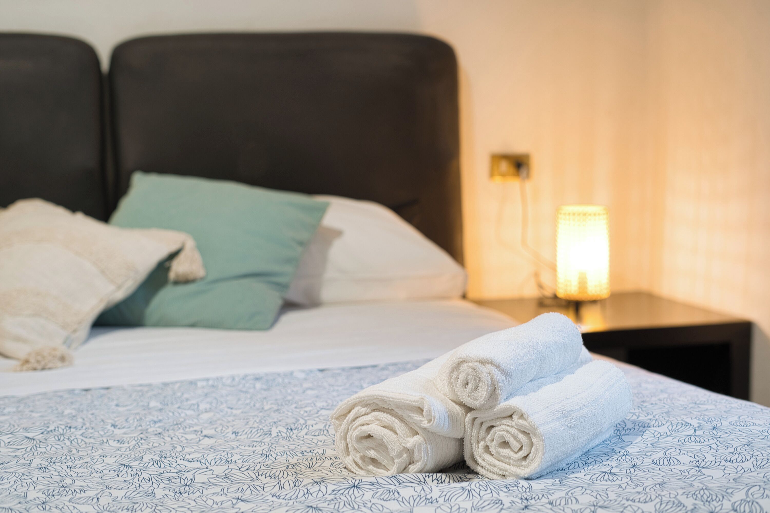 Un lit bien fait, avec des serviettes pliées, un coussin vert et un coussin blanc.