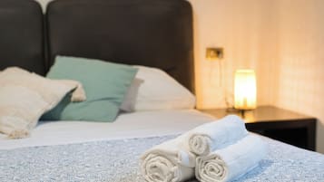 Cama bem arrumada com toalhas dobradas, um travesseiro verde e um travesseiro branco.