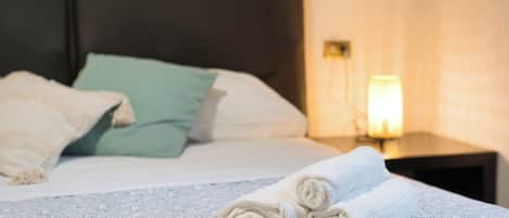 A neatly made bed with rolled towels, a green pillow, and a white pillow.
