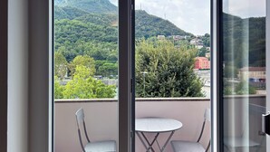 Ein Balkon mit zwei Stühlen und einem Tisch, mit Blick auf eine gebirgige Landschaft mit Gebäuden.