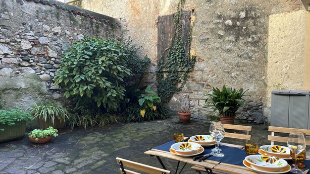 Un área de comedor al aire libre con paredes de piedra, plantas en macetas y una mesa para dos, con platos, cubiertos y vasos.