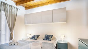 Un dormitorio con una cama, dos mesitas de noche, un armario y una ventana con cortinas.
