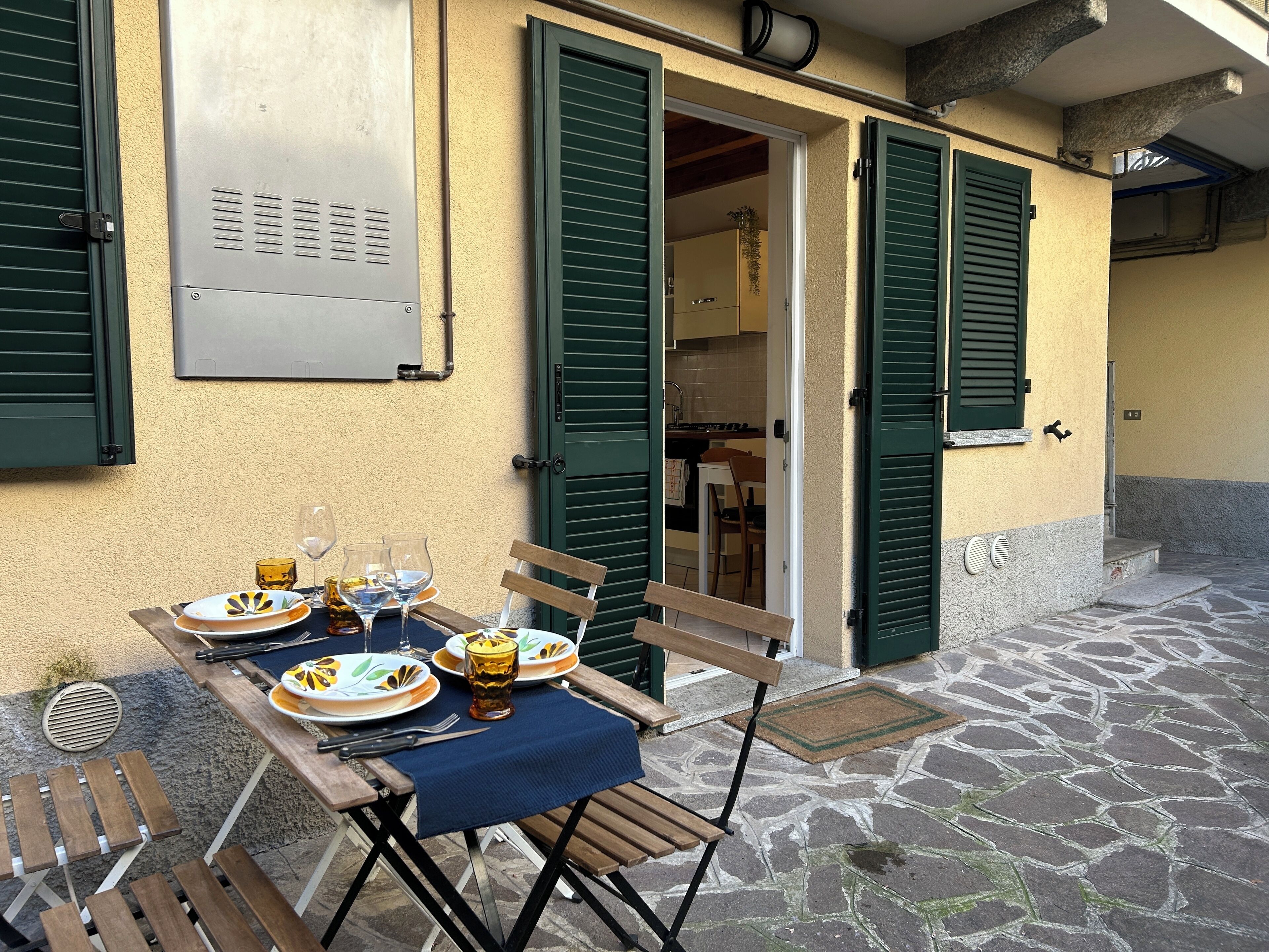 An outdoor dining area with a table set for two, a bench, and a view into the kitchen.