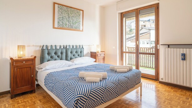 A bedroom with a bed, wooden nightstands, a window with a view, and a radiator.