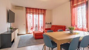 A modern living room with a wooden dining table, blue chairs, a red sofa, and a TV mounted on the wall.