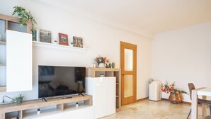 A modern living room with a flat-screen TV, wooden shelves, a door, and a small table with a chair. - Lecco Isola - Top Apartment near Viscontea Island (Lecco)