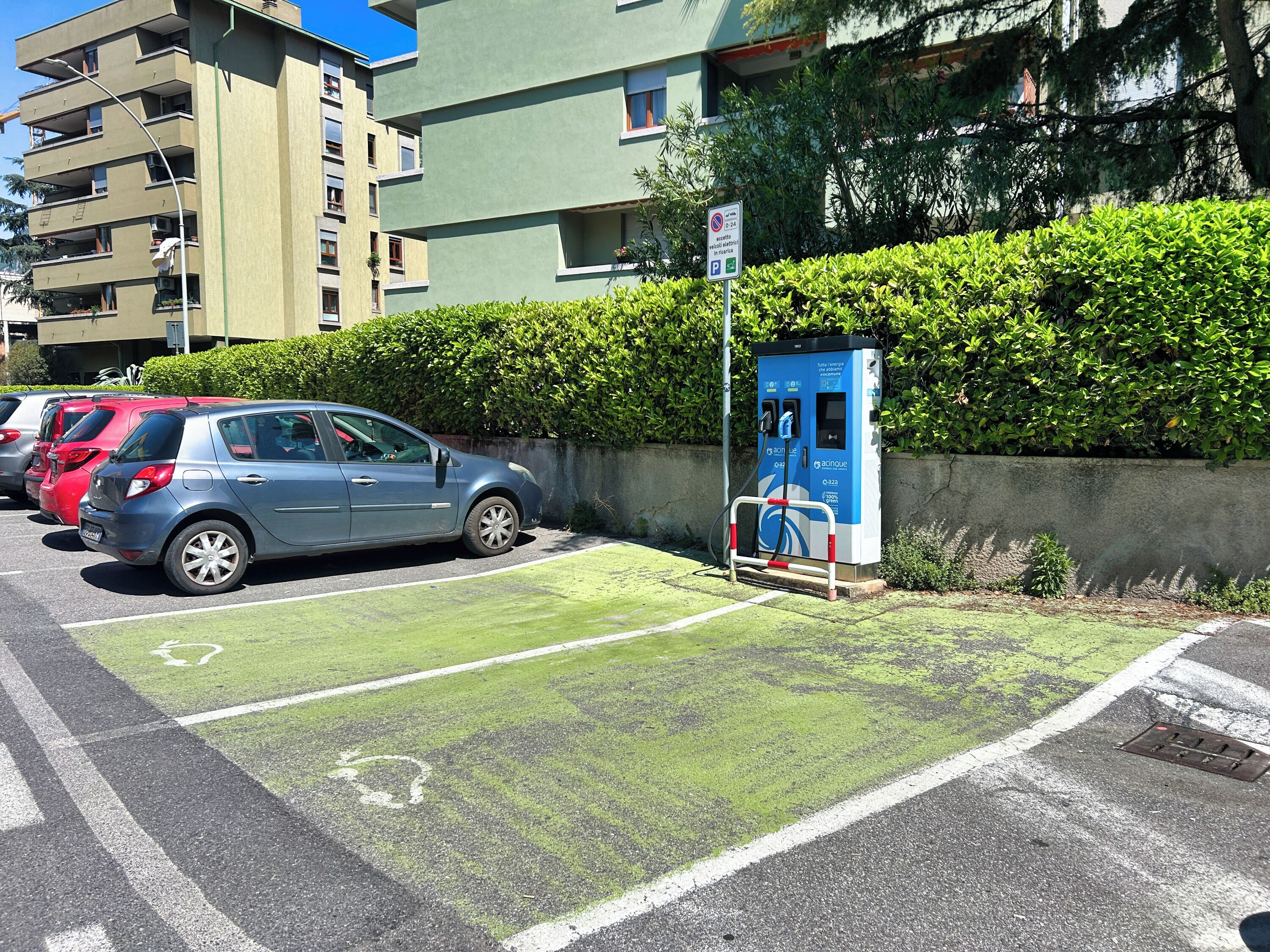 A parking area with electric vehicle charging stations, a blue car, and a building in the background.