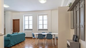 Ein Zimmer mit Holzboden, einem Türkis-sofa, einem weißen Tisch mit blauen Stühlen und einem Holzkabinett mit Haken.