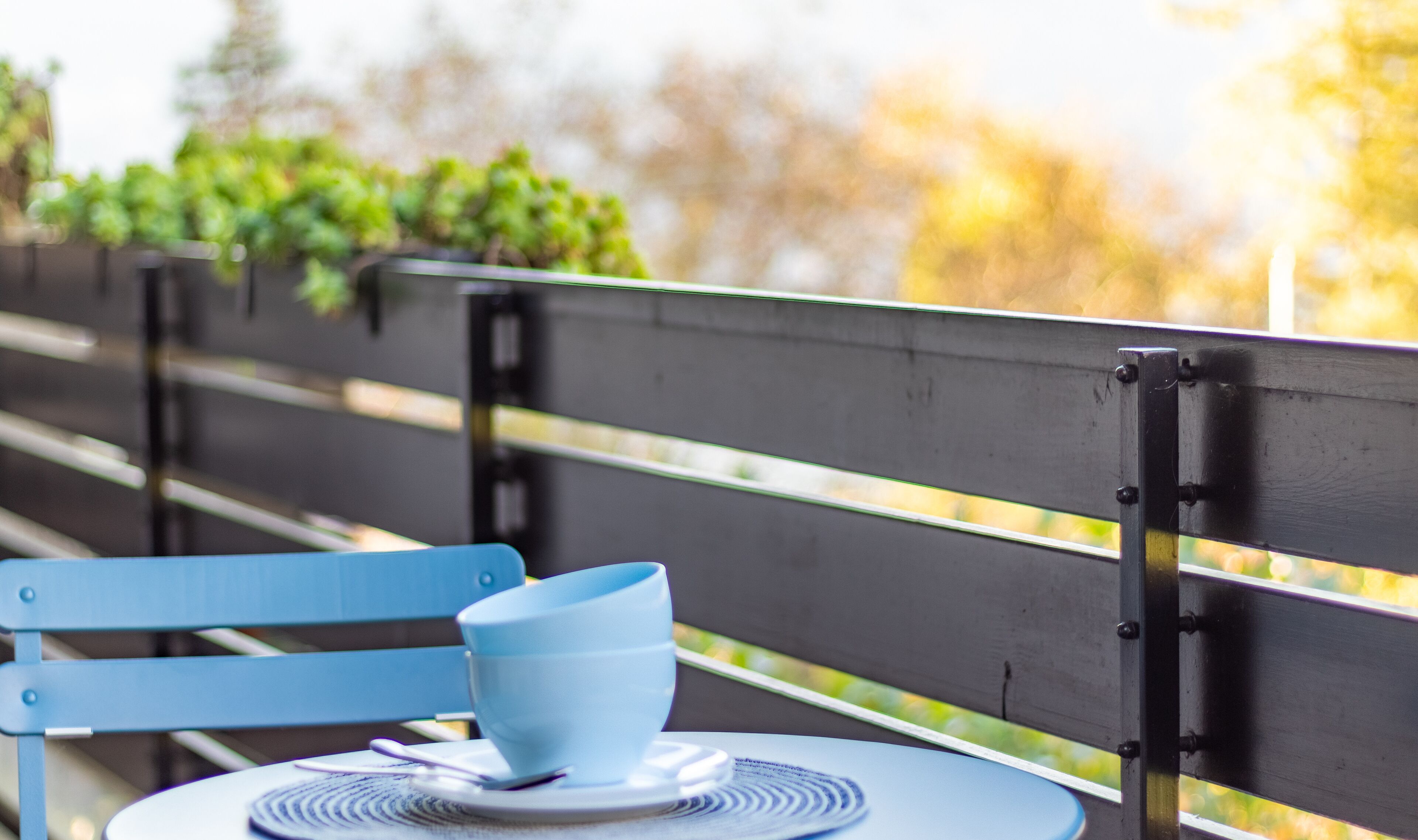 Ein blauer Stuhl mit einem weißen Tisch und einer blauen Tasse darauf, platziert auf einer Bank mit einer schwarzen Rückenlehne.