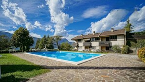 Une maison à deux étages avec une piscine, une terrasse en pierre et une vue sur les montagnes.