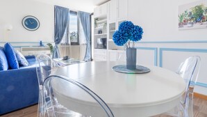 Un espace repas moderne avec une table ronde blanche, des chaises transparentes et un centre de table floral bleu.
