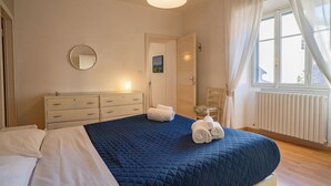A bedroom with a large bed, a bedside table, a dresser, a window with curtains, and a radiator. - Riva Granda - Falcone (Mandello del Lario)