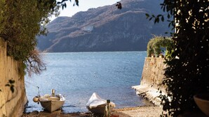 A lakeside scene with boats docked along a rocky shore, surrounded by hills and vegetation. - Riva Granda - Falcone (Mandello del Lario)