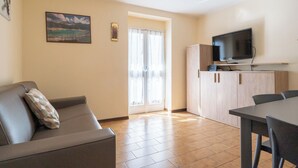 Sala de estar con sofá y mesa de comedor, cocina con televisión y armarios, y una puerta que da al exterior.