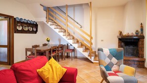 A living room with a wooden staircase, a dining table with chairs, a red sofa, and a patterned armchair.