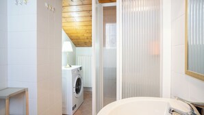 A modern bathroom with a white sink, wooden ceiling, and a washing machine in the background.