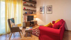 A living room with a red sofa, a wooden chair, a television, a bookshelf, and a small table with a lamp.