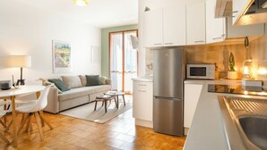 A modern kitchen with a refrigerator, microwave, and stove. There is a dining area with a table and chairs, and a sofa in the living room. - Relaxing Lake Gem - One Bedroom Apartment, Sleeps 4 (Perledo)
