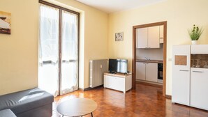 A compact living space with a sofa, a small table, a TV, a kitchen area with cabinets, and a sliding door. - ValleyHideaway with private garden near Como lake (Taceno)