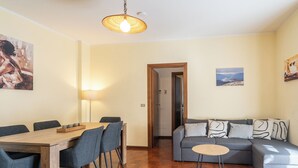 A living room with a wooden dining table, blue chairs, a gray sofa with patterned cushions, a small round table, and a hanging light fixture. - ValleyHideaway with private garden near Como lake (Taceno)