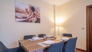 A dining area with a wooden table set for four, surrounded by blue chairs. A painting hangs above the table, and a floor lamp is on to the right. - ValleyHideaway with private garden near Como lake (Taceno)