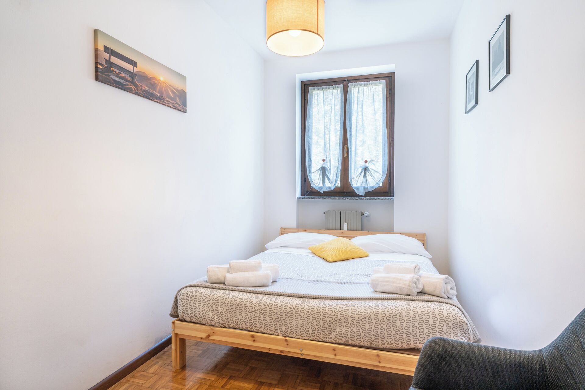 A small, neatly arranged bedroom with a single bed, a window with curtains, and a picture on the wall.