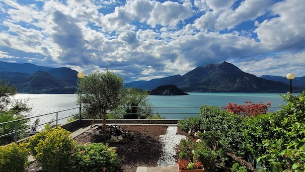 A scenic view of a lake with mountains in the background, a pathway with greenery, and a parked car.